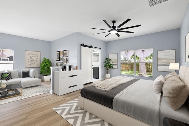 bedroom with light wood finished floors, visible vents, ensuite bathroom, a barn door, and ceiling fan