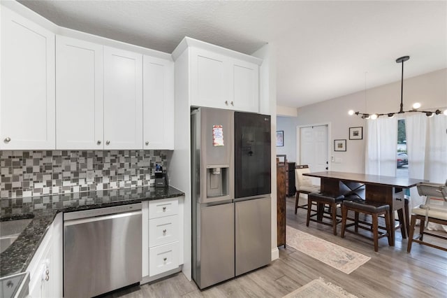 kitchen with white cabinets, decorative backsplash, appliances with stainless steel finishes, decorative light fixtures, and light wood-style floors