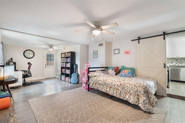 bedroom featuring a textured ceiling, a barn door, wood finished floors, visible vents, and a ceiling fan