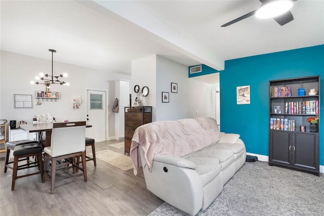 living room with visible vents, baseboards, beamed ceiling, light wood-style floors, and ceiling fan with notable chandelier