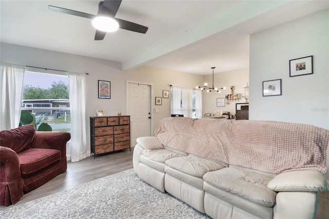 living area featuring light wood-type flooring, beam ceiling, and ceiling fan with notable chandelier