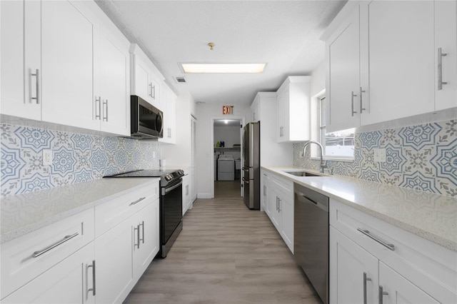 kitchen featuring stainless steel appliances, light wood-style flooring, white cabinets, a sink, and washer and dryer