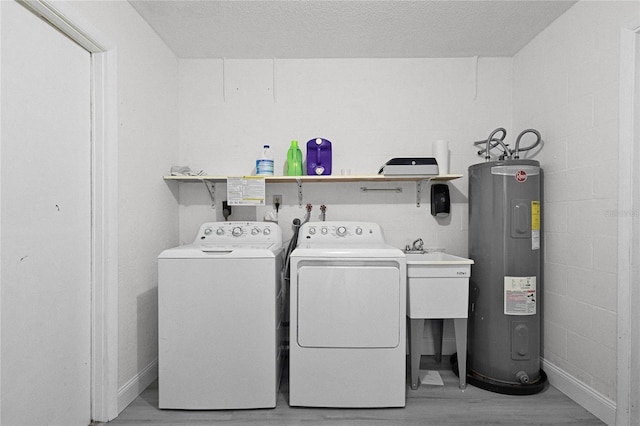 laundry room with concrete block wall, light wood-style floors, electric water heater, laundry area, and independent washer and dryer