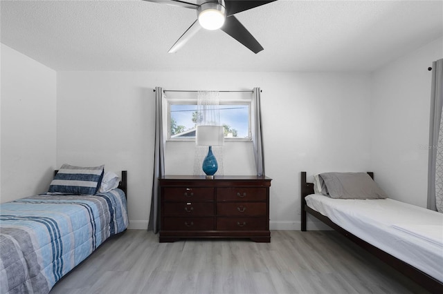 bedroom featuring a textured ceiling, baseboards, light wood-style flooring, and a ceiling fan