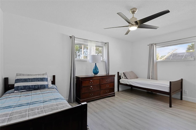 bedroom with a textured ceiling, ceiling fan, light wood finished floors, and multiple windows