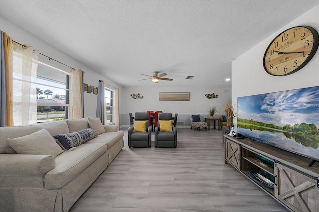 living area featuring light wood-style flooring, visible vents, ceiling fan, and a textured ceiling