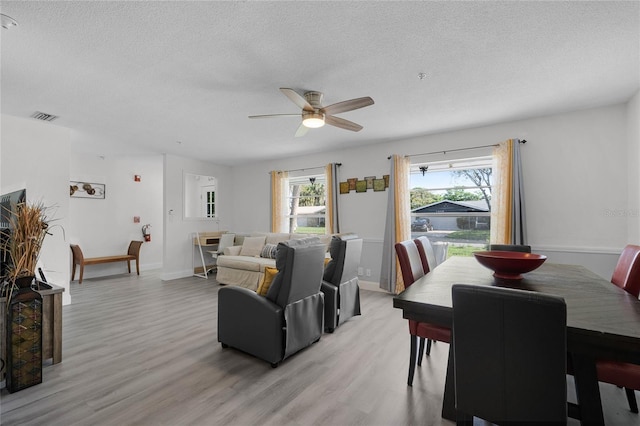 living room featuring light wood finished floors, visible vents, baseboards, a ceiling fan, and a textured ceiling