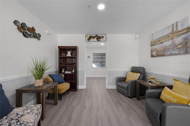 living area featuring a textured ceiling, baseboards, and light wood-style floors