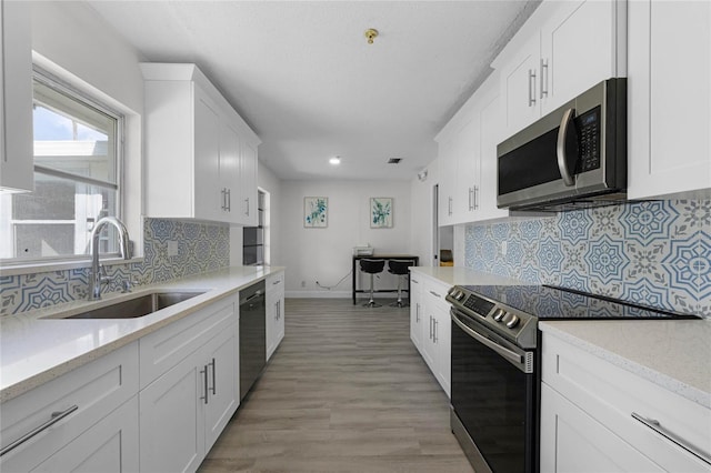 kitchen with appliances with stainless steel finishes, white cabinetry, a sink, and light wood-style flooring