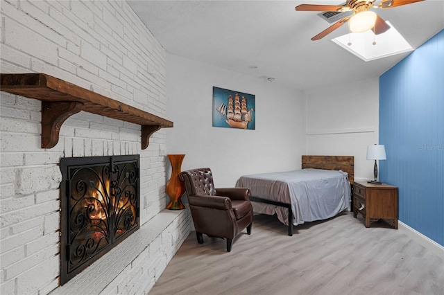 bedroom with a brick fireplace, light wood-style flooring, and a ceiling fan