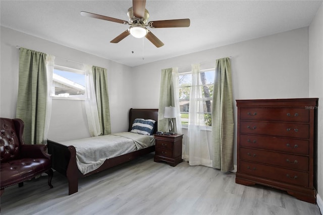 bedroom featuring light wood finished floors, multiple windows, a ceiling fan, and a textured ceiling