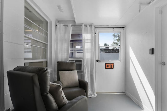 living area with finished concrete floors, visible vents, and cooling unit