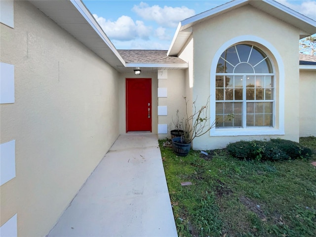 entrance to property with a shingled roof and stucco siding