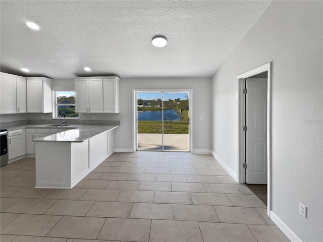 kitchen featuring dark countertops, a wealth of natural light, white cabinets, and a sink