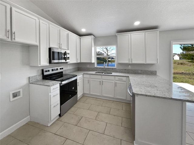 kitchen with appliances with stainless steel finishes, a peninsula, light stone countertops, white cabinetry, and a sink