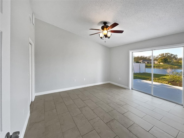 empty room with a textured ceiling, a water view, a ceiling fan, and baseboards