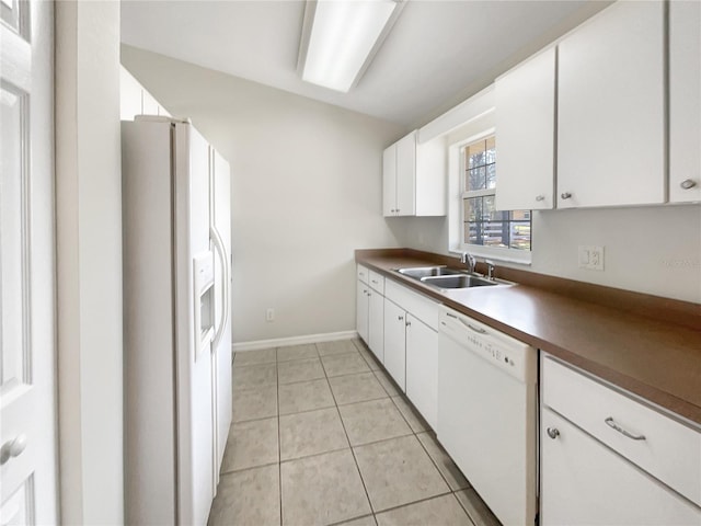 kitchen with light tile patterned floors, dark countertops, white cabinets, a sink, and white appliances