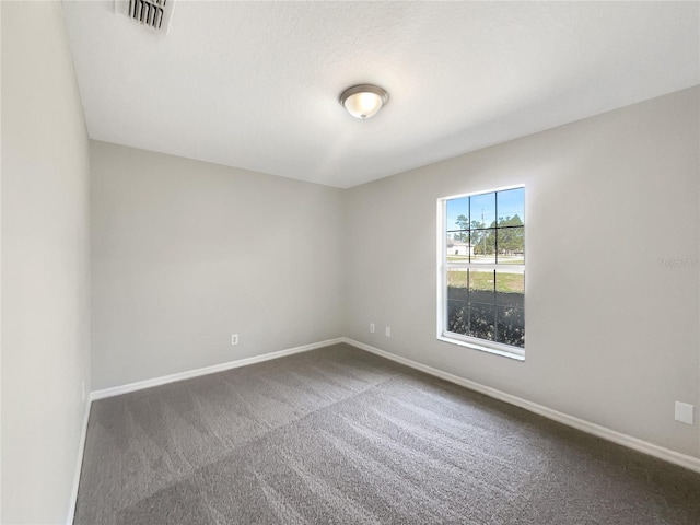 empty room with dark colored carpet, visible vents, and baseboards