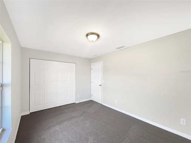 unfurnished bedroom with baseboards, visible vents, dark colored carpet, and a closet