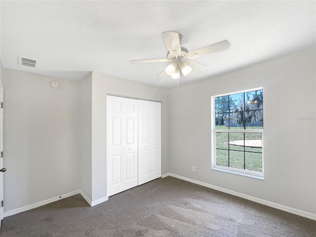 unfurnished bedroom featuring a closet, visible vents, dark carpet, ceiling fan, and baseboards