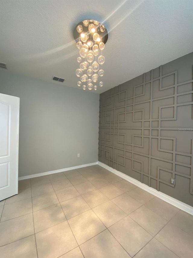 unfurnished room featuring baseboards, light tile patterned flooring, visible vents, and an inviting chandelier