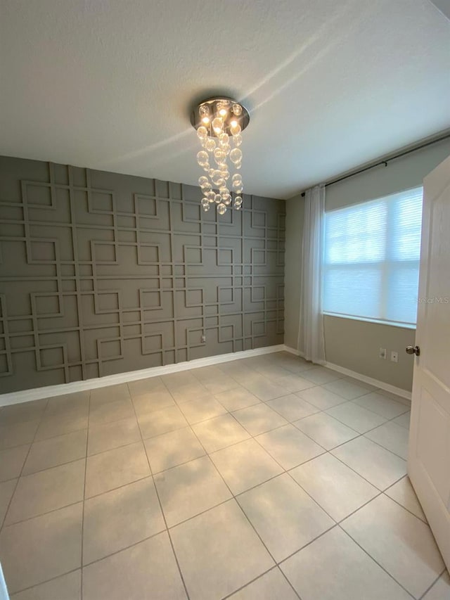 spare room with a textured ceiling, baseboards, light tile patterned flooring, and a notable chandelier