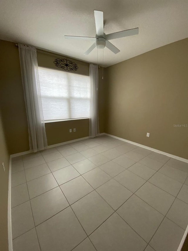 spare room featuring ceiling fan, light tile patterned floors, a textured ceiling, and baseboards