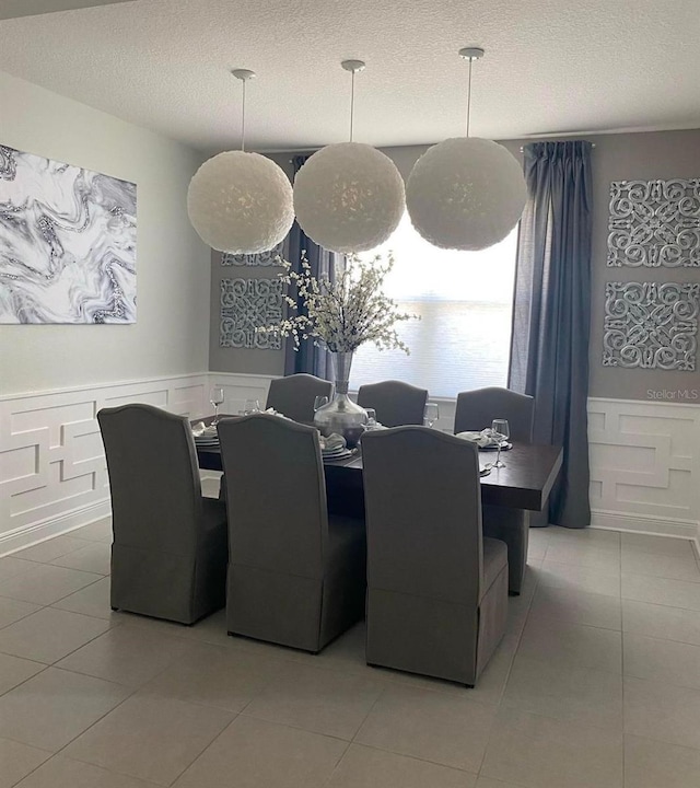 dining space with wainscoting, a decorative wall, a textured ceiling, and light tile patterned flooring