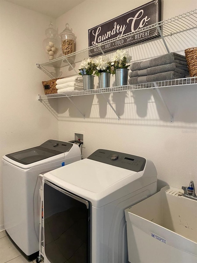 washroom featuring laundry area, washing machine and dryer, light tile patterned floors, and a sink