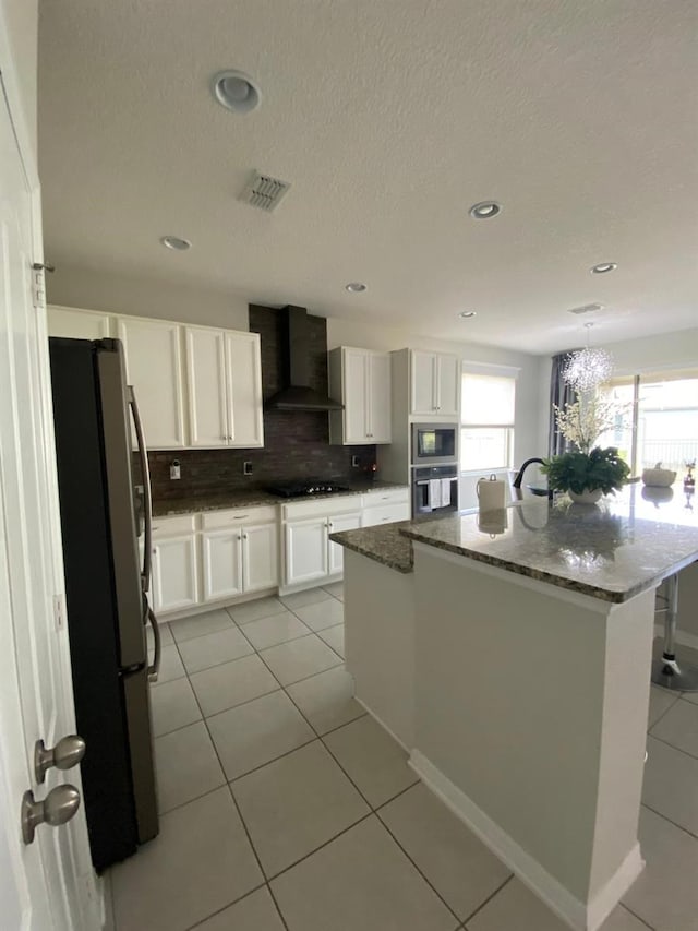 kitchen featuring visible vents, white cabinets, appliances with stainless steel finishes, wall chimney exhaust hood, and dark stone countertops