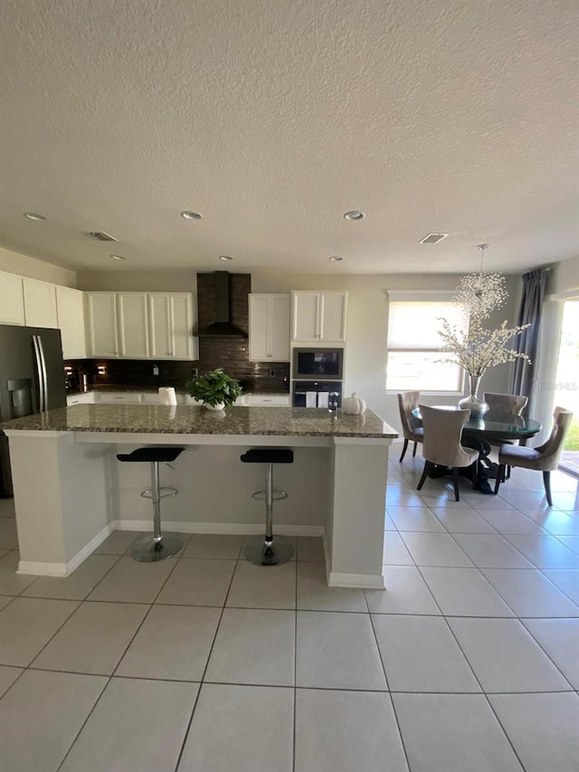 kitchen featuring light tile patterned floors, oven, built in microwave, wall chimney range hood, and white cabinetry