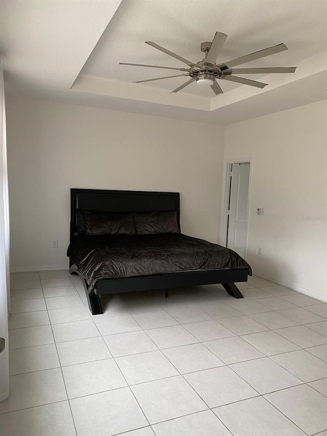 bedroom featuring ceiling fan, a tray ceiling, and light tile patterned floors