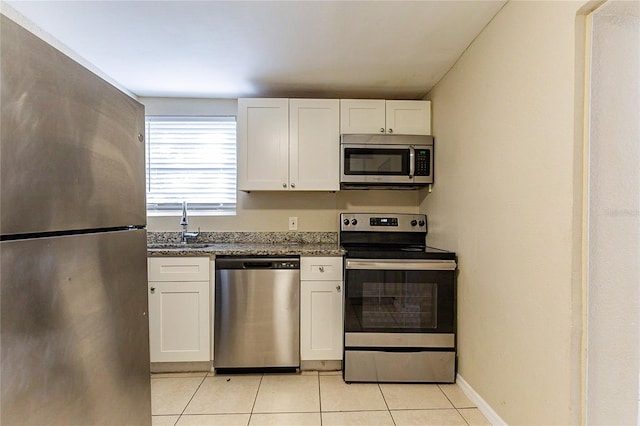 kitchen with light tile patterned floors, a sink, white cabinets, appliances with stainless steel finishes, and dark stone counters