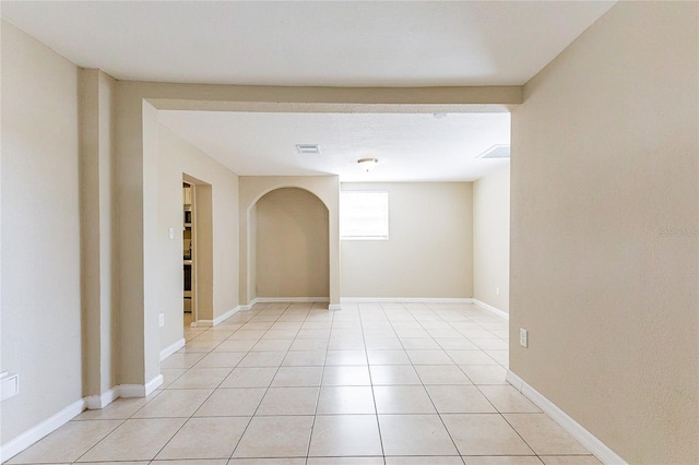 empty room featuring light tile patterned floors, baseboards, visible vents, and arched walkways