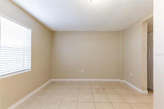 spare room featuring light tile patterned flooring, a textured ceiling, and baseboards