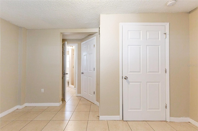 interior space with a textured ceiling, light tile patterned flooring, and baseboards