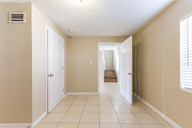 hallway featuring baseboards, visible vents, stairs, a textured ceiling, and light tile patterned flooring