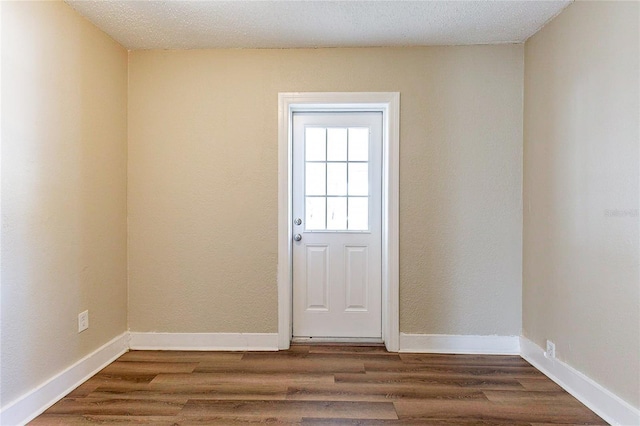 doorway with dark wood-type flooring, a textured ceiling, and baseboards