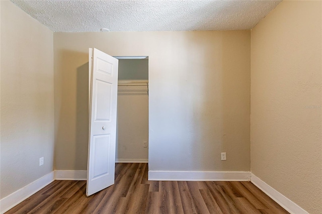 unfurnished bedroom with a closet, dark wood finished floors, a textured ceiling, and baseboards