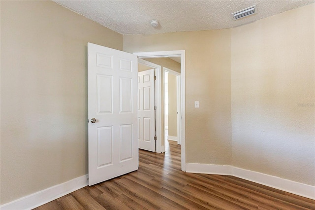 empty room with a textured ceiling, wood finished floors, visible vents, and baseboards