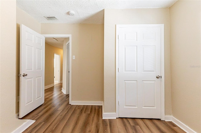 hallway featuring a textured ceiling, wood finished floors, visible vents, and baseboards