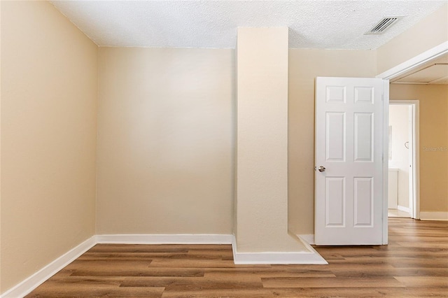 unfurnished room featuring a textured ceiling, wood finished floors, visible vents, and baseboards