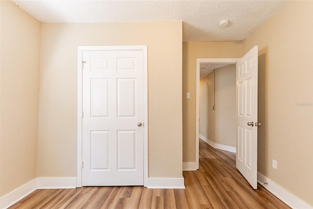 unfurnished bedroom featuring light wood-style floors, baseboards, and a textured ceiling