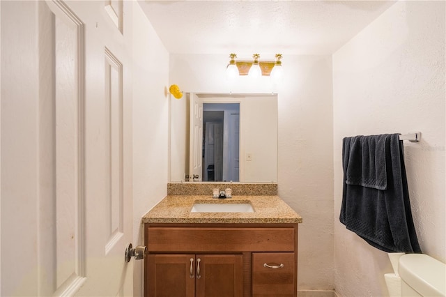 half bathroom with toilet, a textured wall, and vanity