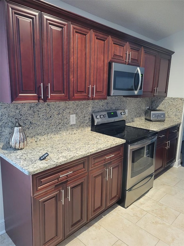 kitchen featuring dark brown cabinets, light stone counters, decorative backsplash, light tile patterned floors, and appliances with stainless steel finishes