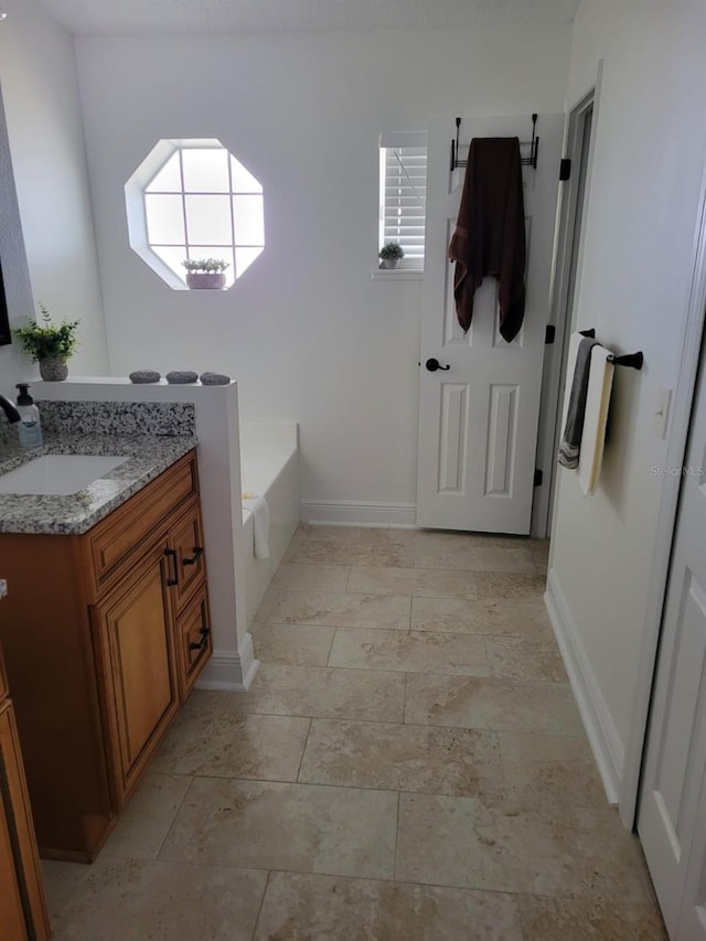 full bathroom featuring vanity, plenty of natural light, a bath, and baseboards