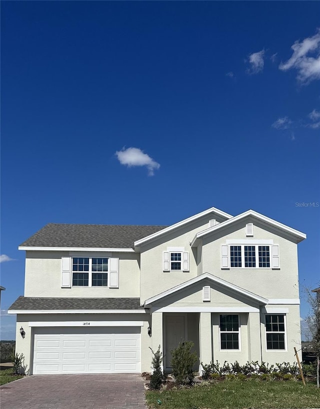 traditional home with an attached garage, roof with shingles, decorative driveway, and stucco siding