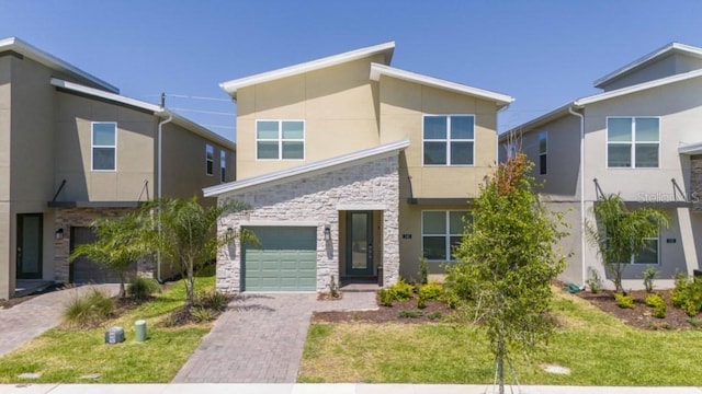 contemporary home with an attached garage, stone siding, decorative driveway, stucco siding, and a front yard