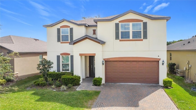 traditional-style home featuring a front lawn, decorative driveway, an attached garage, and stucco siding