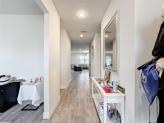 hallway featuring a textured ceiling, baseboards, visible vents, and light wood-style floors